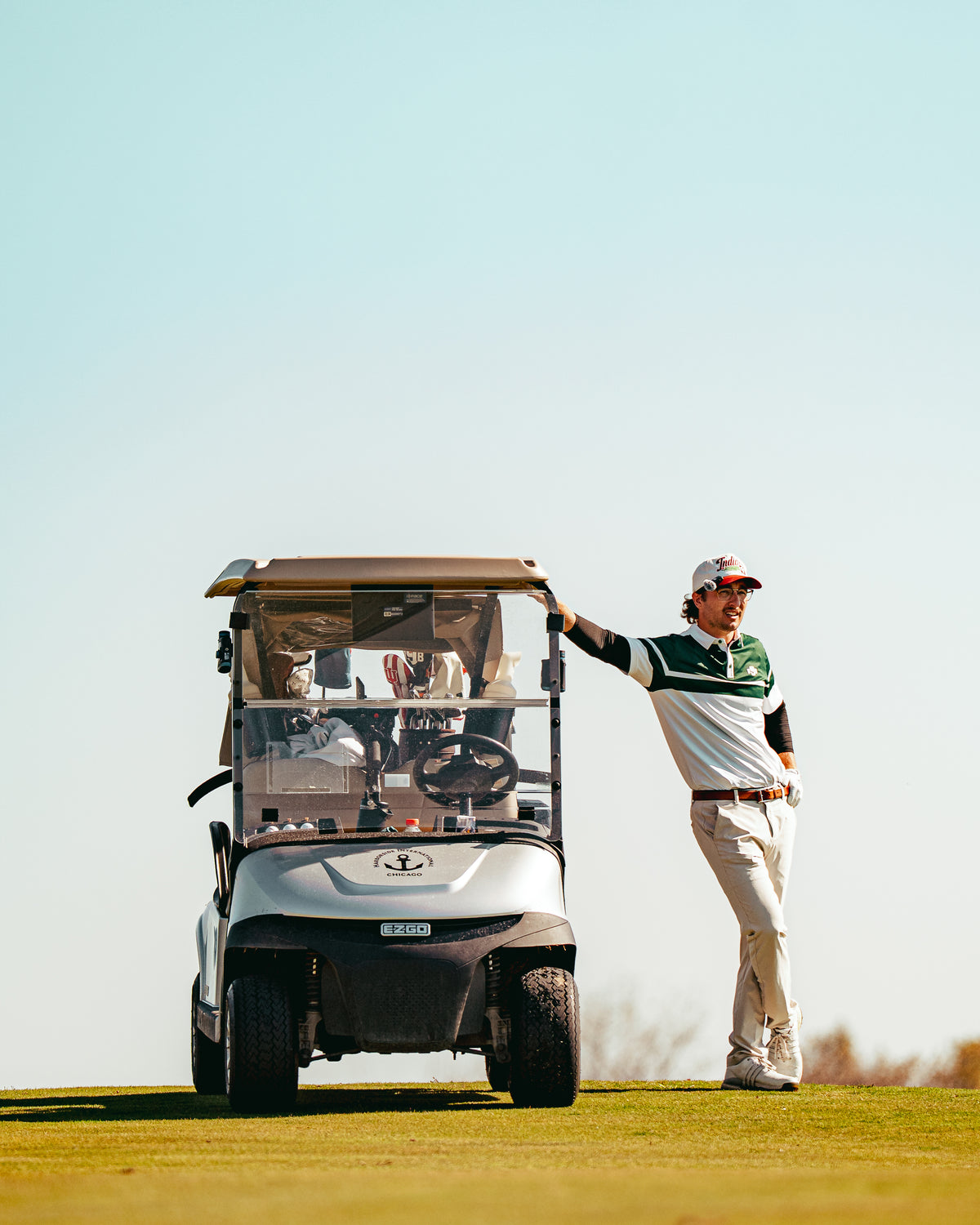 A golfer leaning on a golf cart under a big blue sky