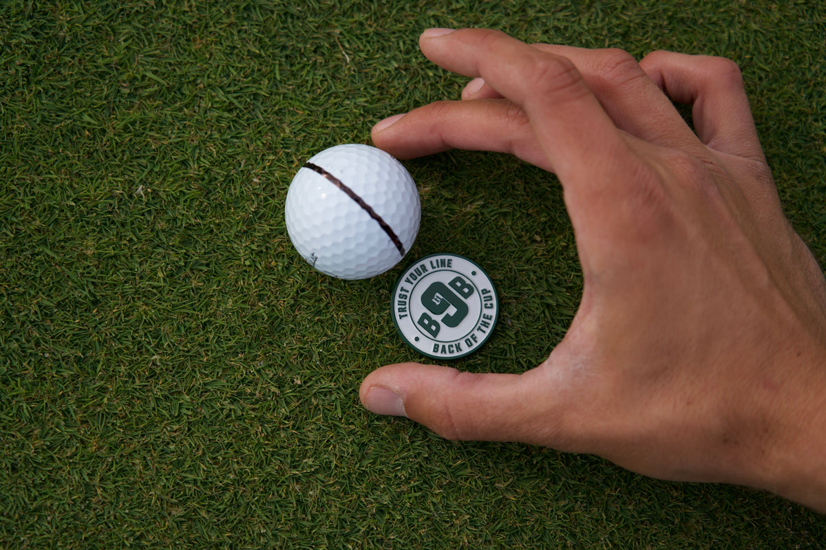 A hand placing the Trust Your Line ballmarker on the green