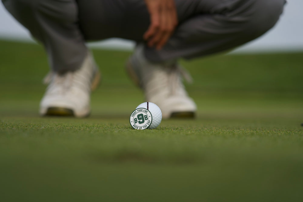 Golfer crouched behind a Back 9 Boys ballmarker on the green